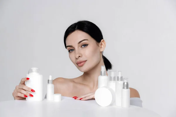 Woman showing cosmetic products branding mockup. Daily skincare and body care routine. Natural cosmetic cream, serum, white bottles packaging, bio organic product.