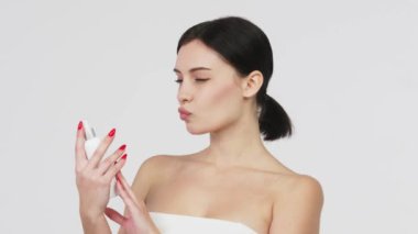 Güzel genç bir kadın banyoda dururken boynuna nemlendirici yüz sisi püskürtüyor. Güzellik, vücut bakımı ve insan konsepti. Gri arka plan üzerinden yüzüne sprey sıkan bir kadın..