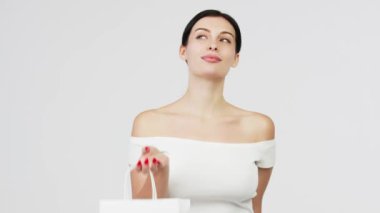 Alışverişi hayal eden kız. Gülümseyen zarif bir kadın, beyaz bir arka planda izole edilmiş kağıt bir alışveriş torbası sunuyor.. 