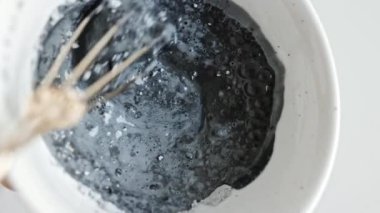 Güzellik uzmanı yüz çamur maskesiyle beyaz bir kaseyi karıştırıyor. Kozmetik kil maskesi. Güzellik salonunda yüz maskesi bileşenlerini karıştırma işlemi.