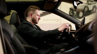 Lüks bir arabada oturan bir adamın yakın çekimi. Mutlu bir araba sahibi modern bir galeride bir araç satın alır. Mutluluk ve pahalı satın alma kavramı.