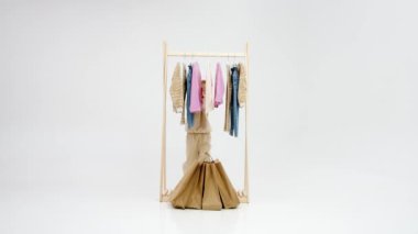 Hafif arka planda paketleri olan küçük bir moda düşkünü. Elbiseli bir askıda çantaları olan sevimli, gülümseyen küçük sarışın kız. Çocuk kıyafetleri ve tarz reklamcılığı konsepti.