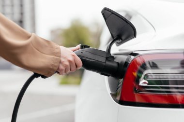 Elektrikli arabayı şarj eden genç kadına yakın durun.