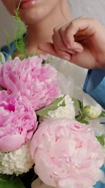 Hafif arka planda ve şakayık demetinde genç bir kadının yakın çekimi. Güzel bir bayan bir buket taze çiçeğin tadını çıkarır. Tatil ve parfüm reklamı kavramı.