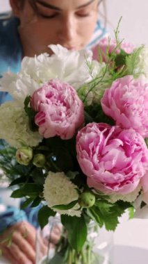 Hafif arka planda ve şakayık demetinde genç bir kadının yakın çekimi. Güzel bir bayan bir buket taze çiçeğin tadını çıkarır. Tatil ve parfüm reklamı kavramı.