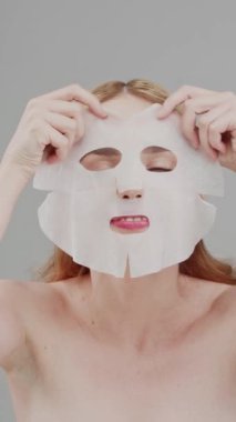 Yüzünde kağıt bir maske olan orta yaşlı bir kadının, kırışıklık önleyici krem ya da gündüz kremi için hazırlanmış güzel bir fotoğrafı. Güzel bir kadın nemlendirici maske takıyor. Kozmetoloji, reklamcılık.