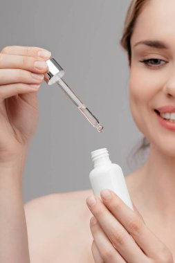 Close-up portrait of a beautiful woman tenderly holding a jar of serum in her hand. Girl in studio on a gray background promote natural skincare. Facial, wellness, young female happy with cosmetics