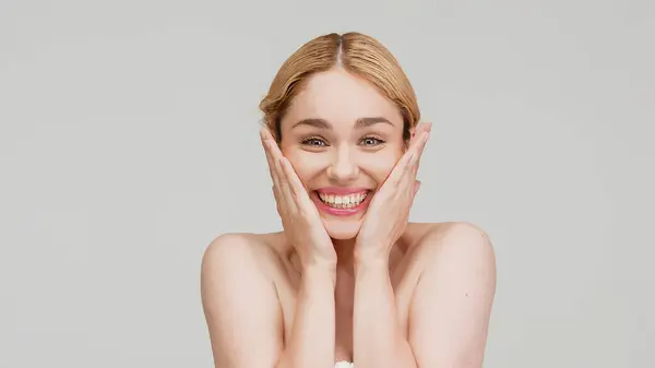 Beauty portrait of young, charming, happy, smiling blonde woman with no makeup and perfect clean, glow skin. Cheerful  female embracing her natural beauty. Isolated on white. Studio background.