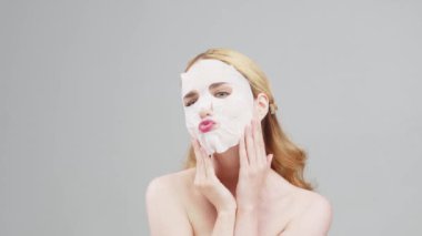 Yüzünde kağıt bir maske olan orta yaşlı bir kadının, kırışıklık önleyici krem ya da gündüz kremi için hazırlanmış güzel bir fotoğrafı. Güzel bir kadın nemlendirici maske takıyor. Kozmetoloji, reklamcılık.