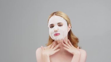 Yüzünde kağıt bir maske olan orta yaşlı bir kadının, kırışıklık önleyici krem ya da gündüz kremi için hazırlanmış güzel bir fotoğrafı. Güzel bir kadın nemlendirici maske takıyor. Kozmetoloji, reklamcılık.