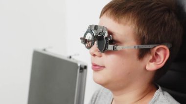 Göz hekimliği kliniğinde küçük mutlu bir hasta. Göz testi, doğruluk için optometrik muayene sırasında deneme çerçevesi deneyen neşeli çocuk.