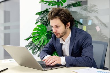 Modern ofiste dizüstü bilgisayara odaklanmış sakallı genç bir tüccar. Finans ve ticaret faaliyetlerini sergilemek için ideal   