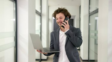 Modern ofis koridorunda kendine güvenen genç bir profesyonel, dizüstü bilgisayar kullanıyor ve kariyerinde ve işinde kendine güvenini sergiliyor..