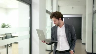 Modern ofis koridorunda kendine güvenen genç bir profesyonel, dizüstü bilgisayar kullanıyor ve kariyerinde ve işinde kendine güvenini sergiliyor..