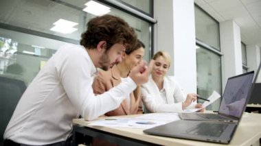 Modern bir ofiste iş arkadaşları birbirlerine danışıyorlar, proje detayları ve finansal stratejiler planlıyorlar. Takım çalışması, proje yönetimi ve iş planlama temaları için ideal.