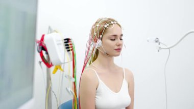 Genç bir kadın modern bir klinikte gelişmiş tıbbi teknoloji ve hasta bakımını gösteren EEG testine tabi tutuluyor. Modern tanı süreçlerini ve sağlık hizmetleri yeniliklerini vurgulamak için ideal.