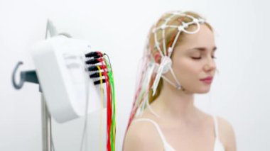 Genç bir kadın modern bir klinikte gelişmiş tıbbi teknoloji ve hasta bakımını gösteren EEG testine tabi tutuluyor. Modern tanı süreçlerini ve sağlık hizmetleri yeniliklerini vurgulamak için ideal.