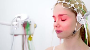 Genç bir kadın modern bir klinikte gelişmiş tıbbi teknoloji ve hasta bakımını gösteren EEG testine tabi tutuluyor. Modern tanı süreçlerini ve sağlık hizmetleri yeniliklerini vurgulamak için ideal.