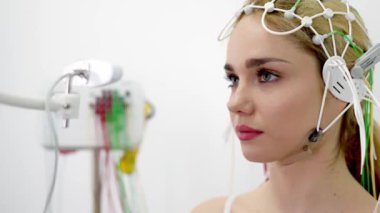 Genç bir kadın modern bir klinikte gelişmiş tıbbi teknoloji ve hasta bakımını gösteren EEG testine tabi tutuluyor. Modern tanı süreçlerini ve sağlık hizmetleri yeniliklerini vurgulamak için ideal.