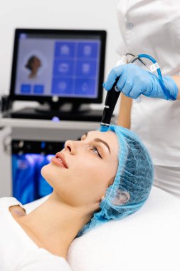 Kozmetik uzmanının elleri, vakum makinesiyle genç bir kadının yüzünü parlatacak ve temizleyecek. Cilt bakımı, gençleştirme ve kozmetoloji kavramı.