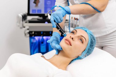 Close-up of cosmetologist hands polishing and cleansing the skin of young woman face using a vacuum machine. Concept of skin care, rejuvenation and cosmetology. clipart