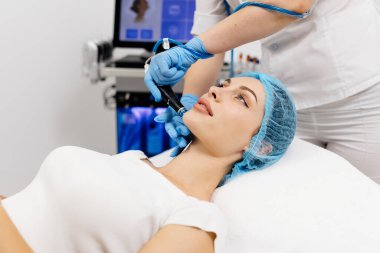 Kozmetik uzmanının elleri, vakum makinesiyle genç bir kadının yüzünü parlatacak ve temizleyecek. Cilt bakımı, gençleştirme ve kozmetoloji kavramı.