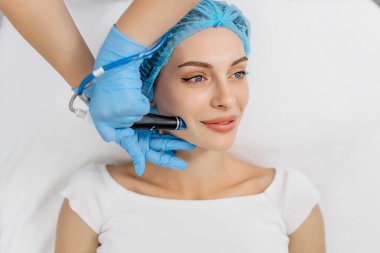 Kozmetik uzmanının elleri, vakum makinesiyle genç bir kadının yüzünü parlatacak ve temizleyecek. Cilt bakımı, gençleştirme ve kozmetoloji kavramı.