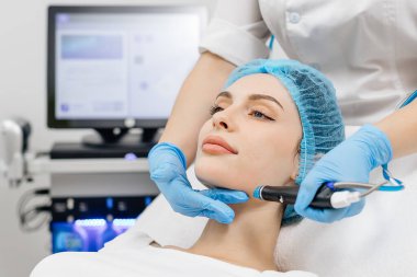 Close-up of cosmetologist hands polishing and cleansing the skin of young woman face using a vacuum machine. Concept of skin care, rejuvenation and cosmetology. clipart