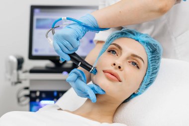 Kozmetik uzmanının elleri, vakum makinesiyle genç bir kadının yüzünü parlatacak ve temizleyecek. Cilt bakımı, gençleştirme ve kozmetoloji kavramı.