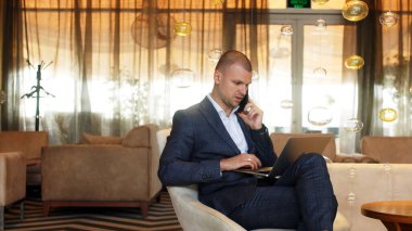 Bir lobide dizüstü bilgisayar üzerinde çalışan odaklanmış bir iş adamı. Bir adam uzak bir iş yerinde akıllı telefondan konuşuyor. Serbest ve çevrimiçi öğrenim kavramı.