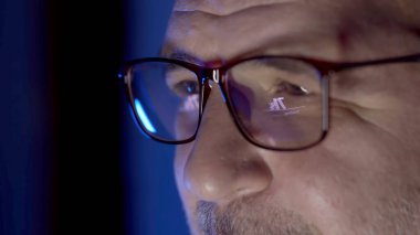 Bilgisayarda çalışan gözlüklü bir geliştiricinin yakın çekimi. Gözlüklerdeki kod ve analizlerin yansımaları siber güvenlik ve yazılım geliştirmede uzmanlığı vurguluyor.