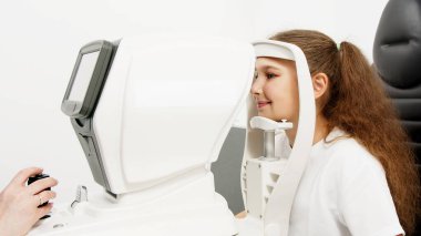 Küçük bir hasta, bir göz hastalıkları kliniğinde modern teşhis ekipmanları kullanan profesyonel bir optometrist tarafından göz testine tabi tutuluyor..