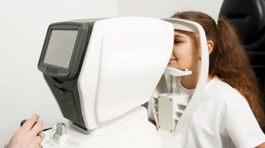Küçük bir hasta, bir göz hastalıkları kliniğinde modern teşhis ekipmanları kullanan profesyonel bir optometrist tarafından göz testine tabi tutuluyor..