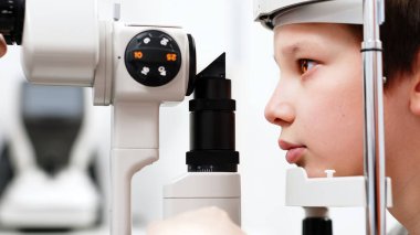 Yarık lamba kullanan çocuğun incelenmesi. Mikroskop ve odaklanmış ışık kaynağı. Merceğin durumunu belirlemek için gözün yüksek hassaslıkta incelenmesi için bir cihaz..