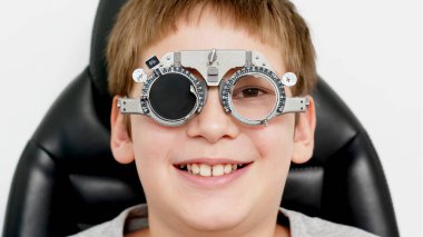 Göz hekimliği kliniğinde küçük bir hasta. Göz testi, doğruluk için optometrik muayene sırasında deneme çerçevesi deneyen neşeli çocuk.