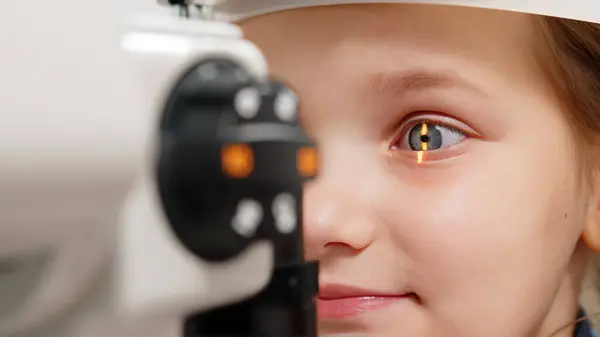 Pediatrik bir göz doktoru küçük bir kızın gözlerini inceliyor. Oftalmik enstrüman. Dikkatli tanı ve çocukların göz sağlığı için bakım.