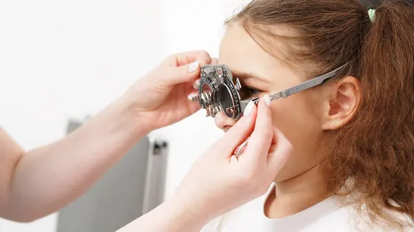 Küçük bir hasta, bir göz hastalıkları kliniğinde modern teşhis ekipmanları kullanan profesyonel bir optometrist tarafından göz testine tabi tutuluyor..