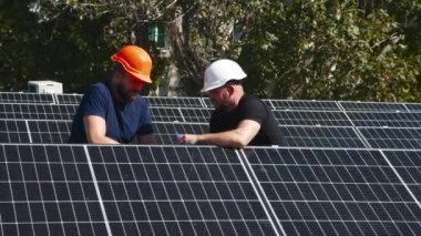 Güneş panellerinin kurulumu, bağlantısı ve montajı. İki işçi güneş panellerini bağlıyor. Teknisyenler metal standa güneş panelleri kuruyor. Bir evin çatısına PV güneş panelleri kuran işçiler.
