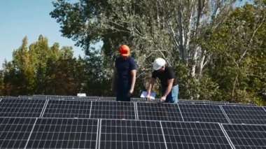 Güneş panellerinin kurulumu, bağlantısı ve montajı. İki işçi güneş panellerini bağlıyor. Teknisyenler metal standa güneş panelleri kuruyor. Bir evin çatısına PV güneş panelleri kuran işçiler.