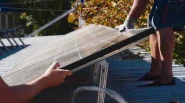 Güneş panellerinin kurulumu, bağlantısı ve montajı. İki işçi güneş panellerini bağlıyor. Teknisyenler metal standa güneş panelleri kuruyor. Bir evin çatısına PV güneş panelleri kuran işçiler.