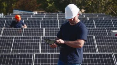 Güneş panellerinin kurulumu, bağlantısı ve montajı. İki işçi güneş panellerini bağlıyor. Teknisyenler metal standa güneş panelleri kuruyor. Bir evin çatısına PV güneş panelleri kuran işçiler.