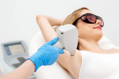 Modern bir klinikte kozmetik uzmanı lazerle saç aldırıyor. Genç bir kadın tüysüz ve pürüzsüz cilt için profesyonel tedavi görüyor.