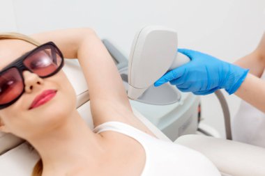 Modern bir klinikte kozmetik uzmanı lazerle saç aldırıyor. Genç bir kadın tüysüz ve pürüzsüz cilt için profesyonel tedavi görüyor.