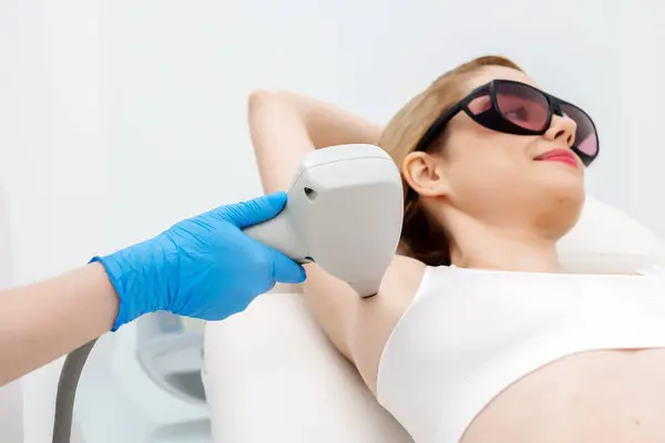 Modern bir klinikte kozmetik uzmanı lazerle saç aldırıyor. Genç bir kadın tüysüz ve pürüzsüz cilt için profesyonel tedavi görüyor.