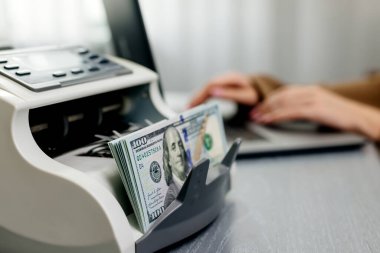 Elektronik para sayma makinesinde dizüstü bilgisayarı ve dolar banknotları olan kadın işçilere yakın çekim, finansal hizmetleri, nakit yönetimini veya döviz kurunu resmetmek için ideal.                           