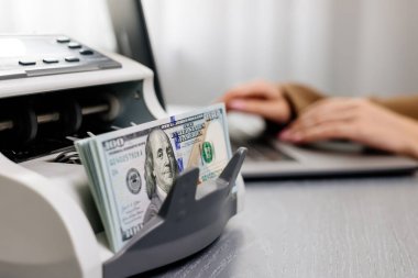 Elektronik para sayma makinesinde dizüstü bilgisayarı ve dolar banknotları olan kadın işçilere yakın çekim, finansal hizmetleri, nakit yönetimini veya döviz kurunu resmetmek için ideal.                           