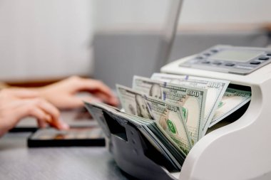 Elektronik para sayma makinesinde dizüstü bilgisayarı ve dolar banknotları olan kadın işçilere yakın çekim, finansal hizmetleri, nakit yönetimini veya döviz kurunu resmetmek için ideal.                           