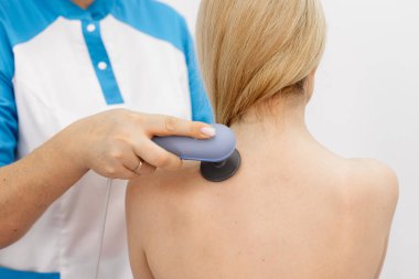 Genç bir kadın modern bir klinikte elektromanyetik terapi görüyor. Tedavi dokuların iyileşmesini hızlandırır, acıyı hafifletir ve kas gelişimini hızlandırır, genel sağlığa katkıda bulunur..