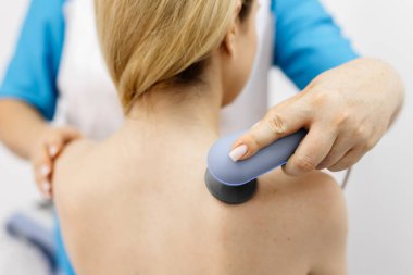 Genç bir kadın modern bir klinikte elektromanyetik terapi görüyor. Tedavi dokuların iyileşmesini hızlandırır, acıyı hafifletir ve kas gelişimini hızlandırır, genel sağlığa katkıda bulunur..