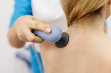 Genç bir kadın modern bir klinikte elektromanyetik terapi görüyor. Tedavi dokuların iyileşmesini hızlandırır, acıyı hafifletir ve kas gelişimini hızlandırır, genel sağlığa katkıda bulunur..